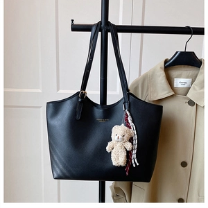 Close-up of black leather tote bag with gold lettering and cute bear charm pendant