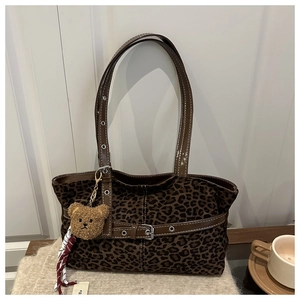 Detail of leopard print tote bag with brown leather straps and a plush bear pendant
