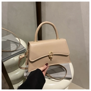 Detail of beige crossbody bag with gold buckle lock on books against grey background