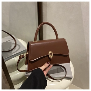 Detail view of a brown trapezoidal handbag with a golden circular metal buckle and strap