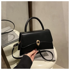 Detailed close-up of a black matte leather trapezoid bag with a unique gold metal clasp