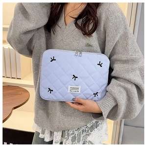 Détail d'une pochette en nylon bleu clair matelassé avec broderie nœud noir et fermeture éclair