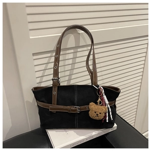 Dettaglio borsa tote in tela nera con cinturini in pelle marrone e ciondolo orso