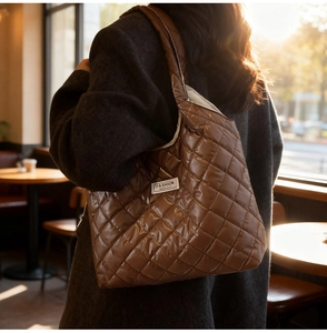 Detail of a brown quilted puffer tote bag with glossy finish and brand label