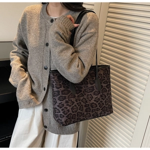 Detail of large leopard print tote bag with black leather straps worn by a model