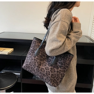 Detail of leopard print tote bag with black leather straps shown on a model