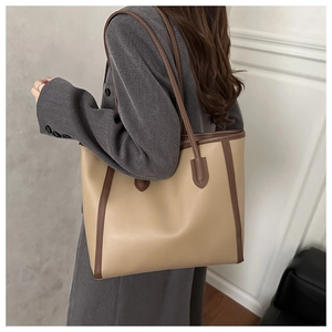 Model wearing a large beige tote bag with dark brown trim and straps for a stylish look