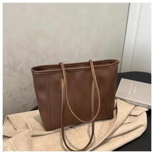 Detail of dark brown leather tote bag styled with beige coat and aesthetic book