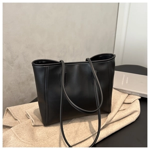 Minimalist black tote bag in faux leather shown with an overcoat and books