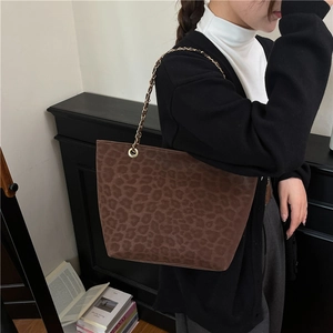 Brown leopard print tote bag with metal chain strap worn by a model in a casual street style