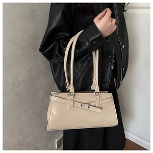 Gros plan d'un sac baguette en cuir beige avec boucles argentées porté à l'épaule