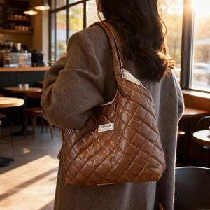Minimalistische gesteppte Tragetasche in Dunkelbraun mit Fashion-Label im sonnigen Café