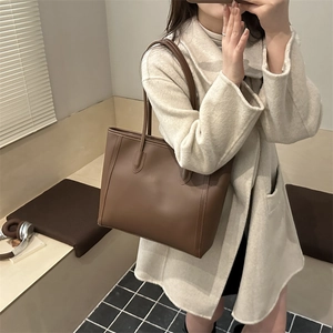 Minimalist brown leather tote bag with shoulder strap shown in a lifestyle setting