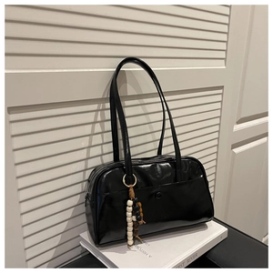 Close-up of black glossy PU leather pillow bag with stylish beaded charm on white books