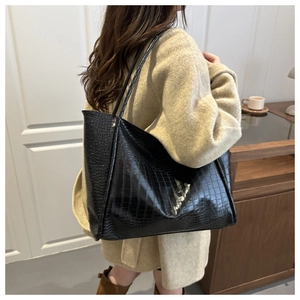 Detail of black crocodile embossed leather tote bag worn by model on shoulder