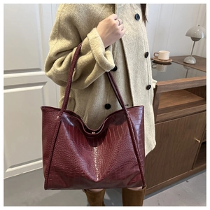 Close-up of a burgundy tote bag featuring premium crocodile embossed leather texture