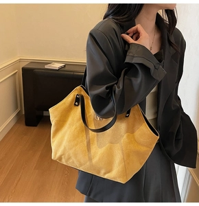 Detail of yellow suede tote bag featuring large diamond stitching and black leather straps