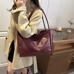 Deep red crocodile embossed tote bag held by model wearing a beige winter coat