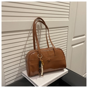 Detail of a brown glossy leather Boston bag with wooden bead charm on white books