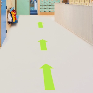 Close-up of green PVC arrow floor decals guiding the path in a modern corridor