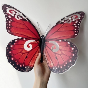 Detalle de una gran mariposa decorativa 3D roja sostenida a mano para mostrar el tamaño