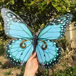 Decoración de pared mariposa 3D azul de 40 cm sostenida a mano en un jardín