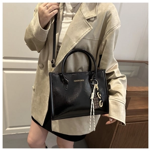 Détail d'un sac cabas en similicuir noir verni avec lettrage doré et bandoulière