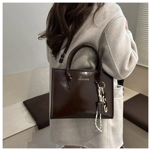 Brown leather tote bag featuring golden lettering and a chocolate-shaped charm detail