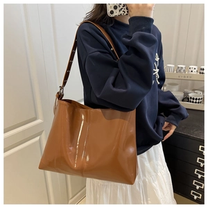 Detail of a brown glossy patent leather tote bag with adjustable strap and metal buckle