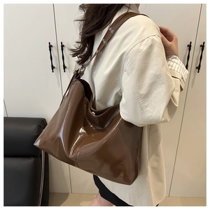 Detail view of large dark brown patent leather hobo bag with eyelet metal strap