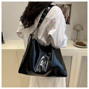 Detail of wide shoulder strap with metal eyelets on a black patent leather tote bag
