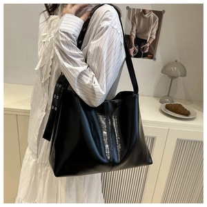 Detail view of black patent leather tote bag with silver eyelets on a wide shoulder strap