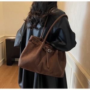 Close-up of matte brown suede tote bag with silver metal buckle and long leather strap