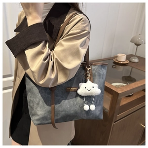 Detail view of a gray-blue tote bag with brown straps and a cute white cloud plush charm