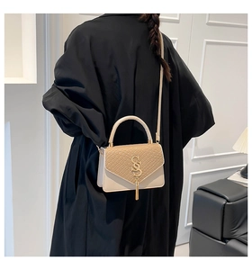 Détail du sac crème avec rabat à texture tissée, logo doré et pendentif à pompon chic