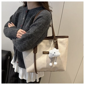 Detail of off-white tote bag featuring dark brown contrast trim and cloud plush charm