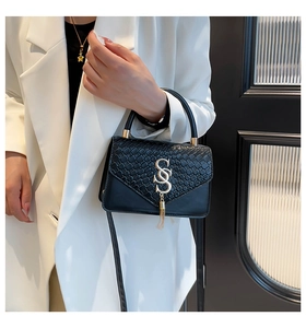 Détail d'un sac à main noir en cuir tressé avec boucle dorée en S porté par un mannequin