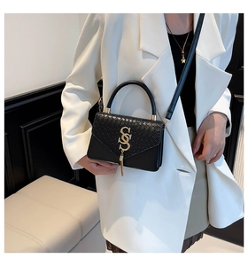 Detail of a chic black crossbody bag with faux crocodile texture and gold hardware on a model
