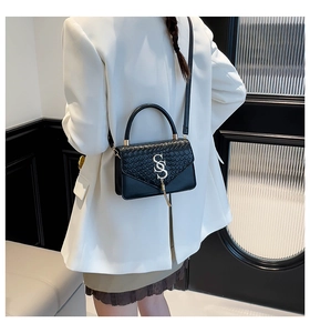 Detail of black woven flap handbag with large silver S-shaped buckle on white suit