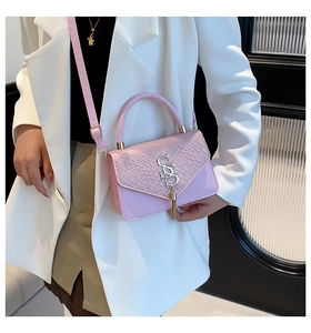 Détail du sac bandoulière rose avec texture crocodile, logo SS doré et pompon élégant