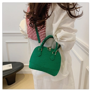 Fashion model wearing a vibrant green crocodile texture shell bag over white shirt