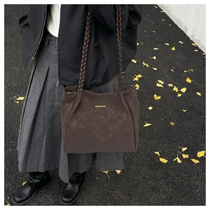 Detail of dark brown matte tote bag with woven handles and gold brand lettering on surface