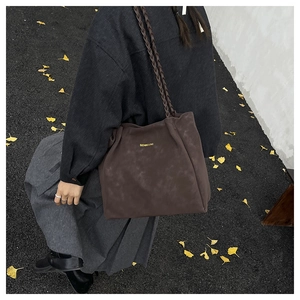 Detail of deep brown tote bag featuring matte leather texture and woven braided shoulder strap