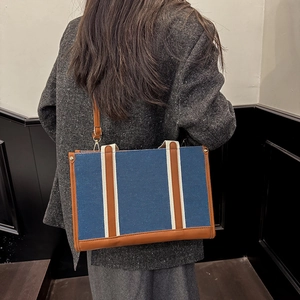 Sac cabas en toile bleue avec finitions en cuir marron porté par un mannequin