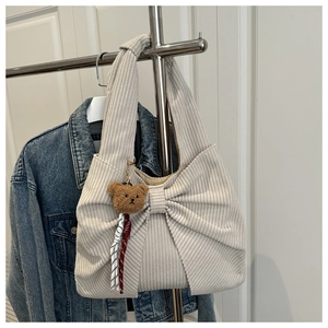 Detail of cream corduroy tote bag featuring a large bow design and a cute plush bear charm