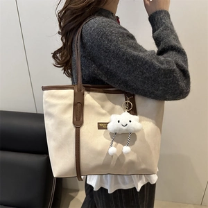 Large beige and brown tote bag with cloud pendant worn on the shoulder by a model