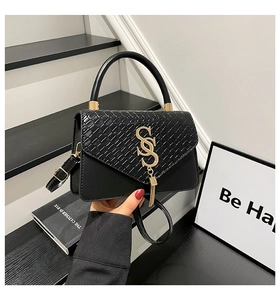 Detalle de bolso bandolera de cuero negro tejido con logo S dorado y borla metálica