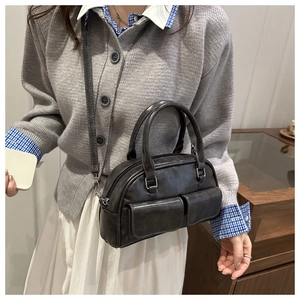 Model wearing a black leather bowling bag with front pockets and crossbody strap