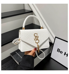 Detalle de bolso bandolera blanco con textura de cocodrilo, hebilla de flecos dorados y asa