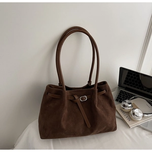 Detail of dark brown suede tote bag with silver buckle and thin straps on a desk